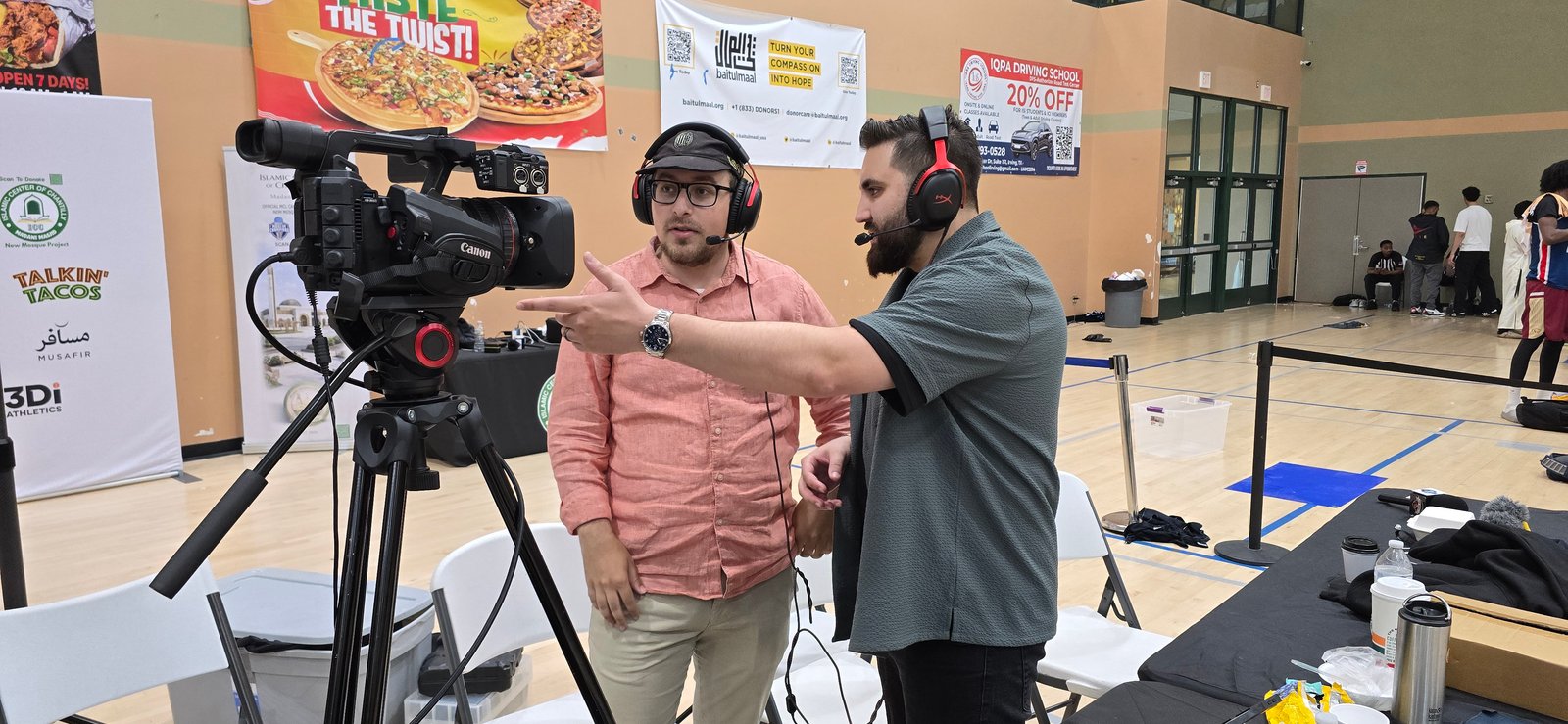 Two broadcast crew members at a production setup courtside, one operating a Canon camera and the other directing